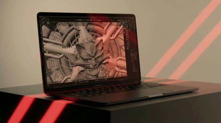 Laptop showing a 3D model in progress on a desk with red lighting